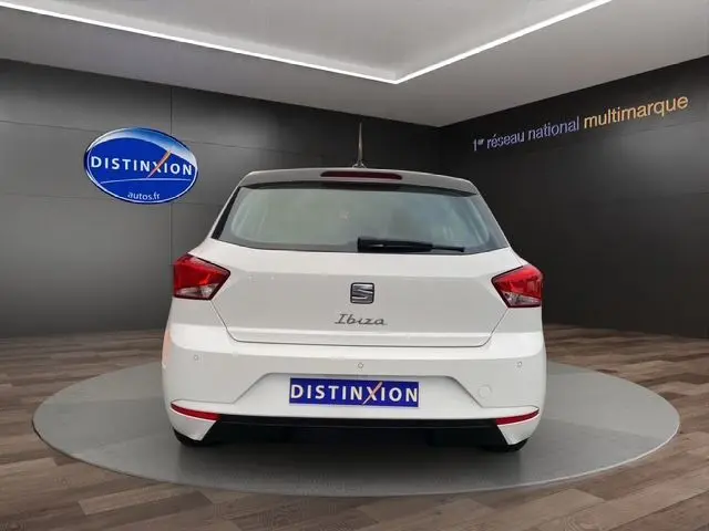 Vue arrière d'une SEAT Ibiza blanche Candy 2023 dans un showroom avec logo Distinxion en arrière-plan.