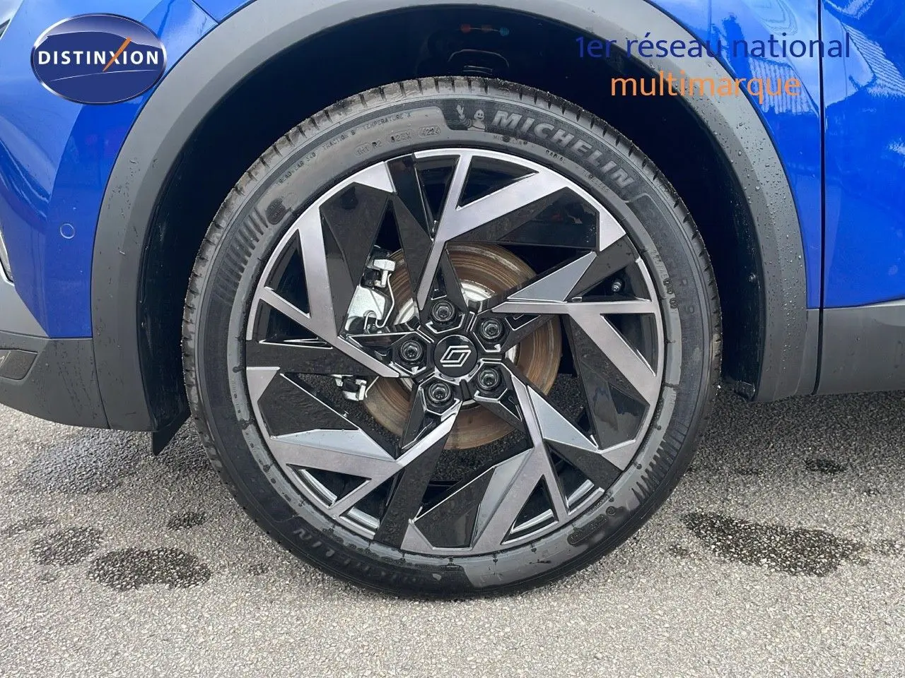 Gros plan sur la roue avant gauche du Renault Captur bleu Iron Metal avec jante alliage noire et argentée au design géométrique.