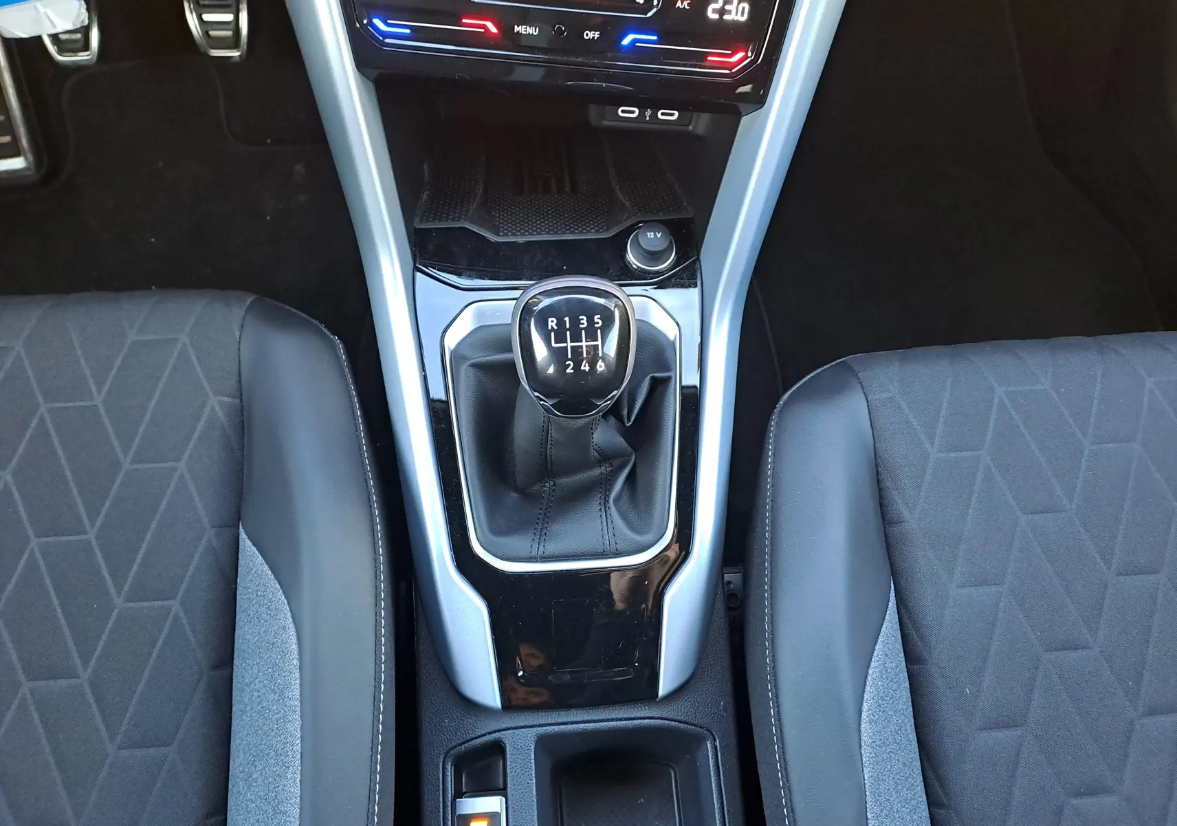 Vue plongeante sur la console centrale du Volkswagen T-Roc gris Ascot, avec levier de vitesses manuel et sièges tissu noir.