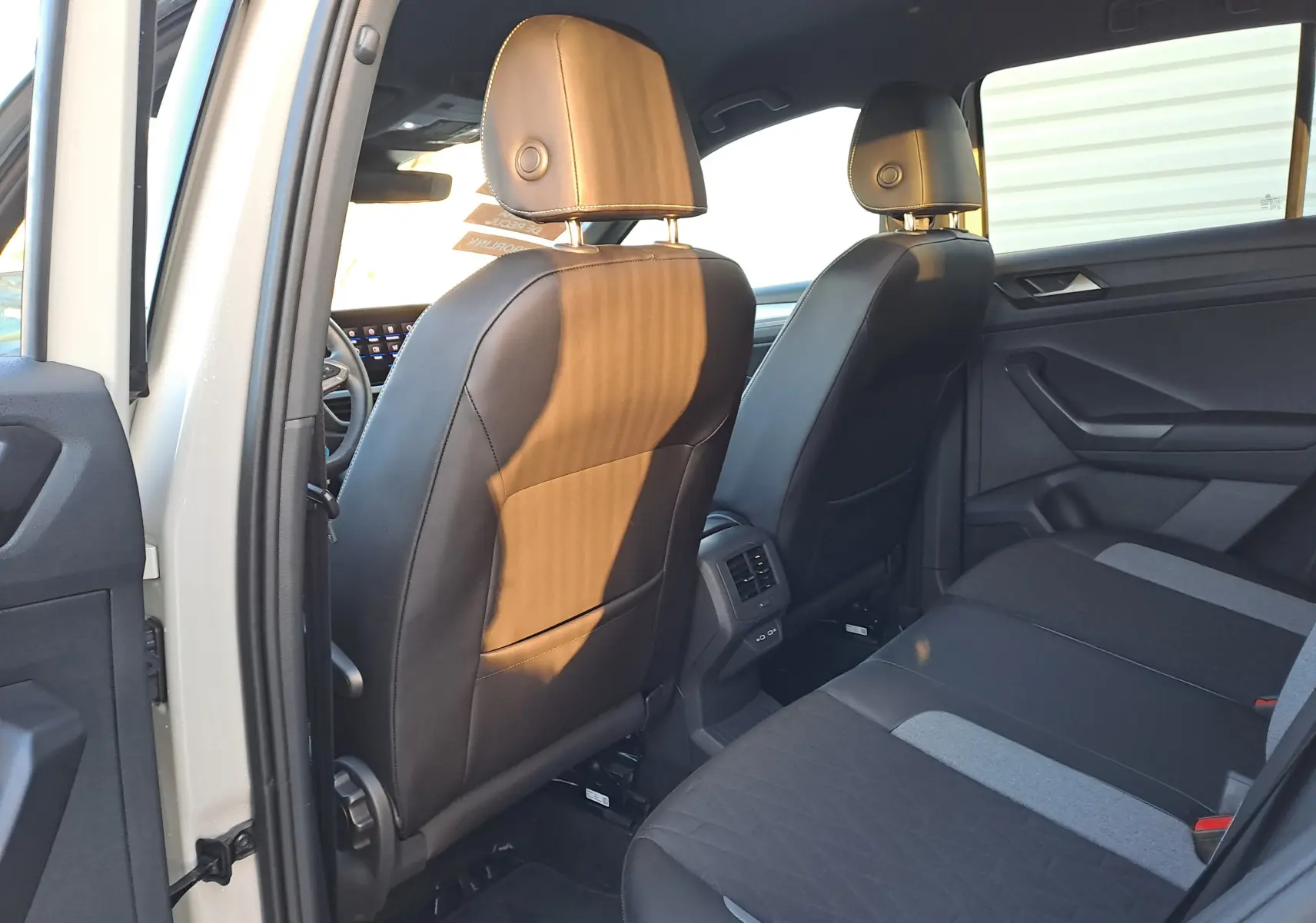 Vue intérieure arrière du Volkswagen T-Roc 2025 gris Ascot, montrant les sièges avant en cuir et la banquette arrière en tissu bicolore.