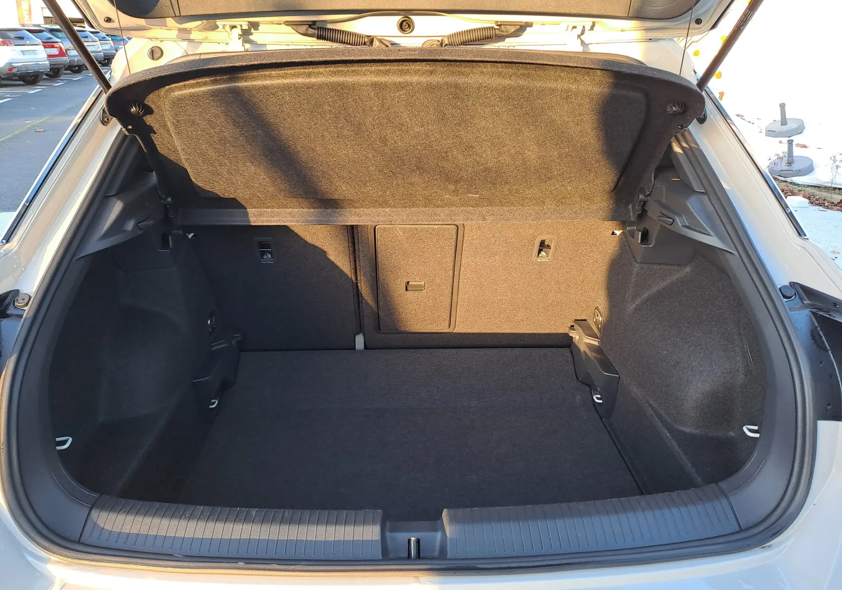 Vue arrière du coffre ouvert du Volkswagen T-Roc gris Ascot 2025, montrant l'espace de rangement et la moquette intérieure noire.