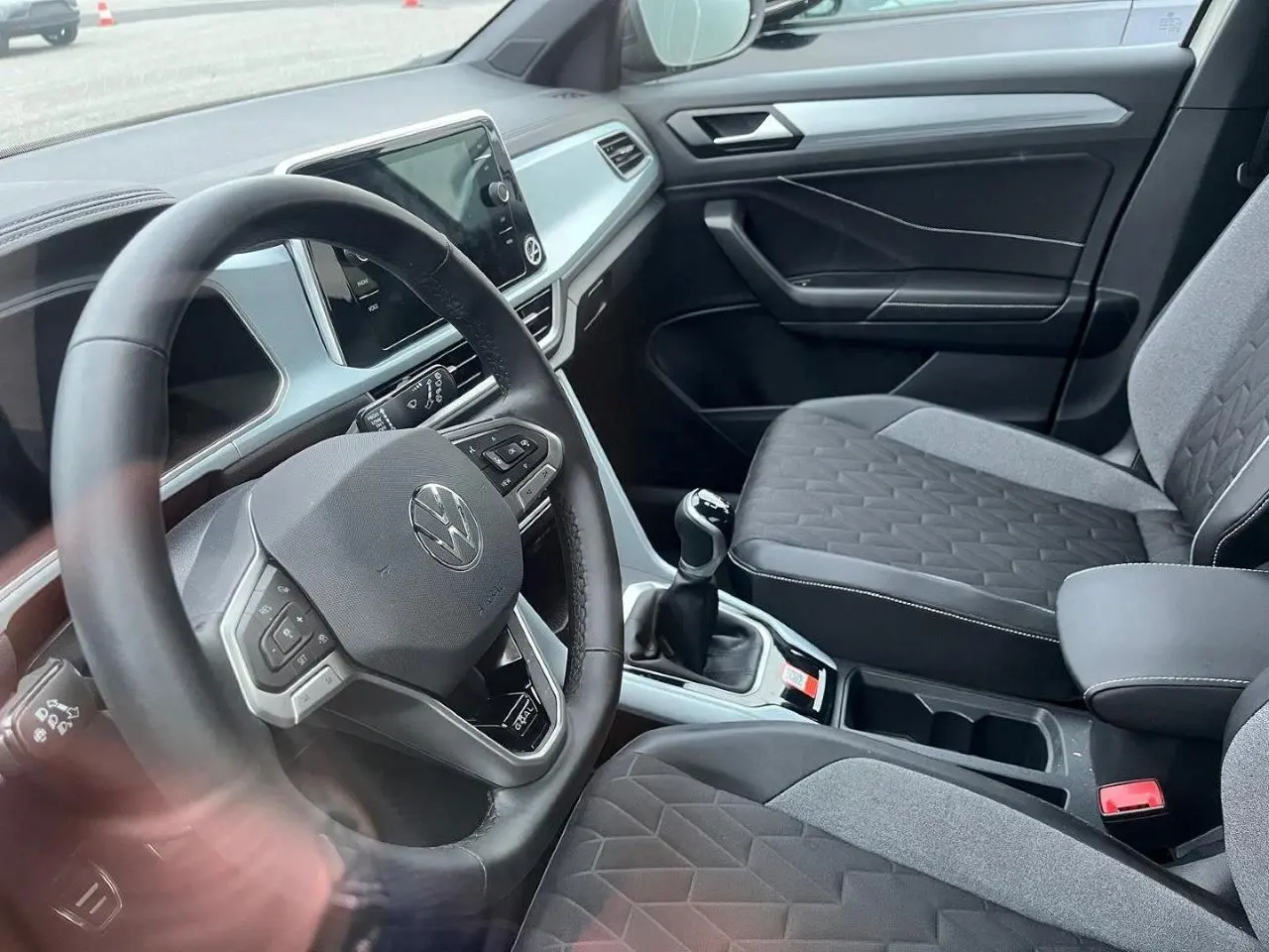 Vue intérieure côté conducteur du Volkswagen T-Roc 2025, avec volant multifonction et sièges tissu gris à motifs géométriques.