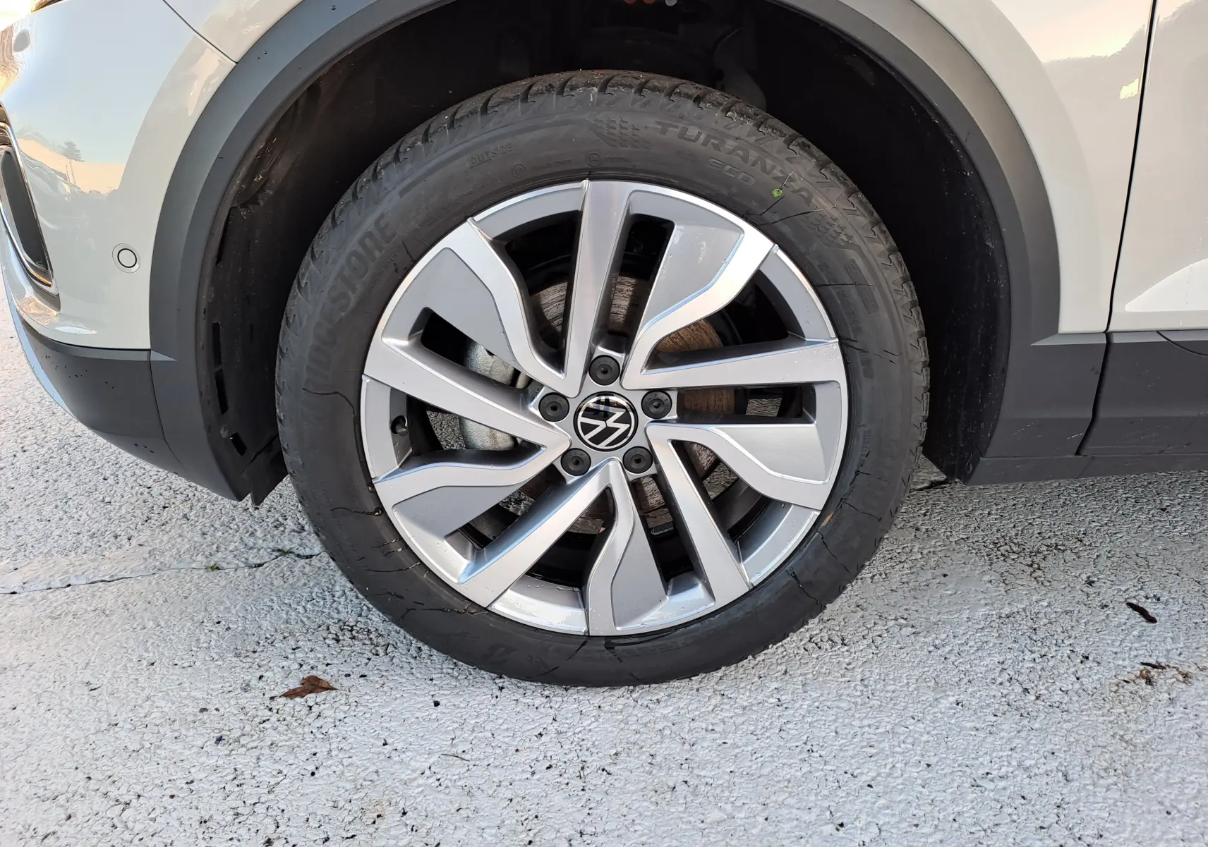 Gros plan sur la roue avant gauche du Volkswagen T-Roc gris Ascot, mettant en valeur la jante alliage au design moderne.