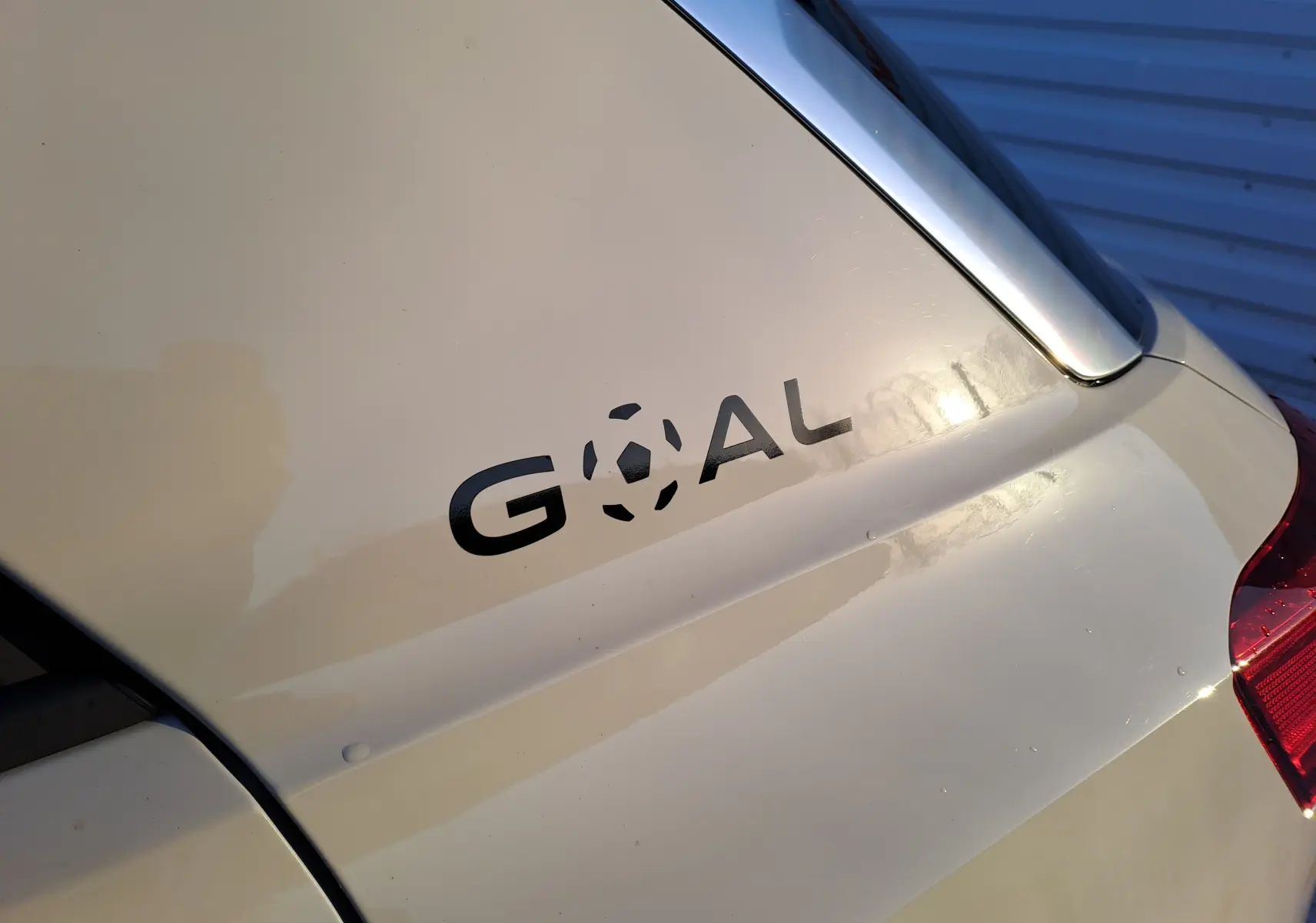 Gros plan sur le coffre gris ascot d'un Volkswagen T-Roc 2025 avec l'inscription noire "GOAL" et partie du feu arrière droit.
