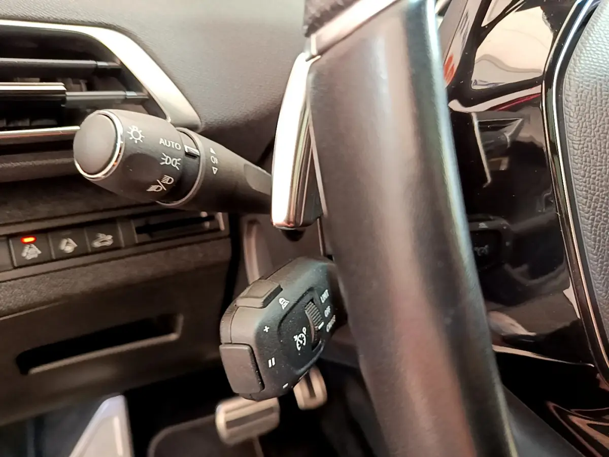 Gros plan sur la commande de régulateur et les commandes d'éclairage à gauche du volant cuir du Peugeot 3008 GT rouge 2021.