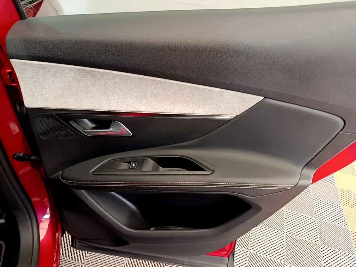 Vue rapprochée de la porte avant gauche rouge du Peugeot 3008 GT avec garniture noire et grise et bouton de fenêtre électrique.