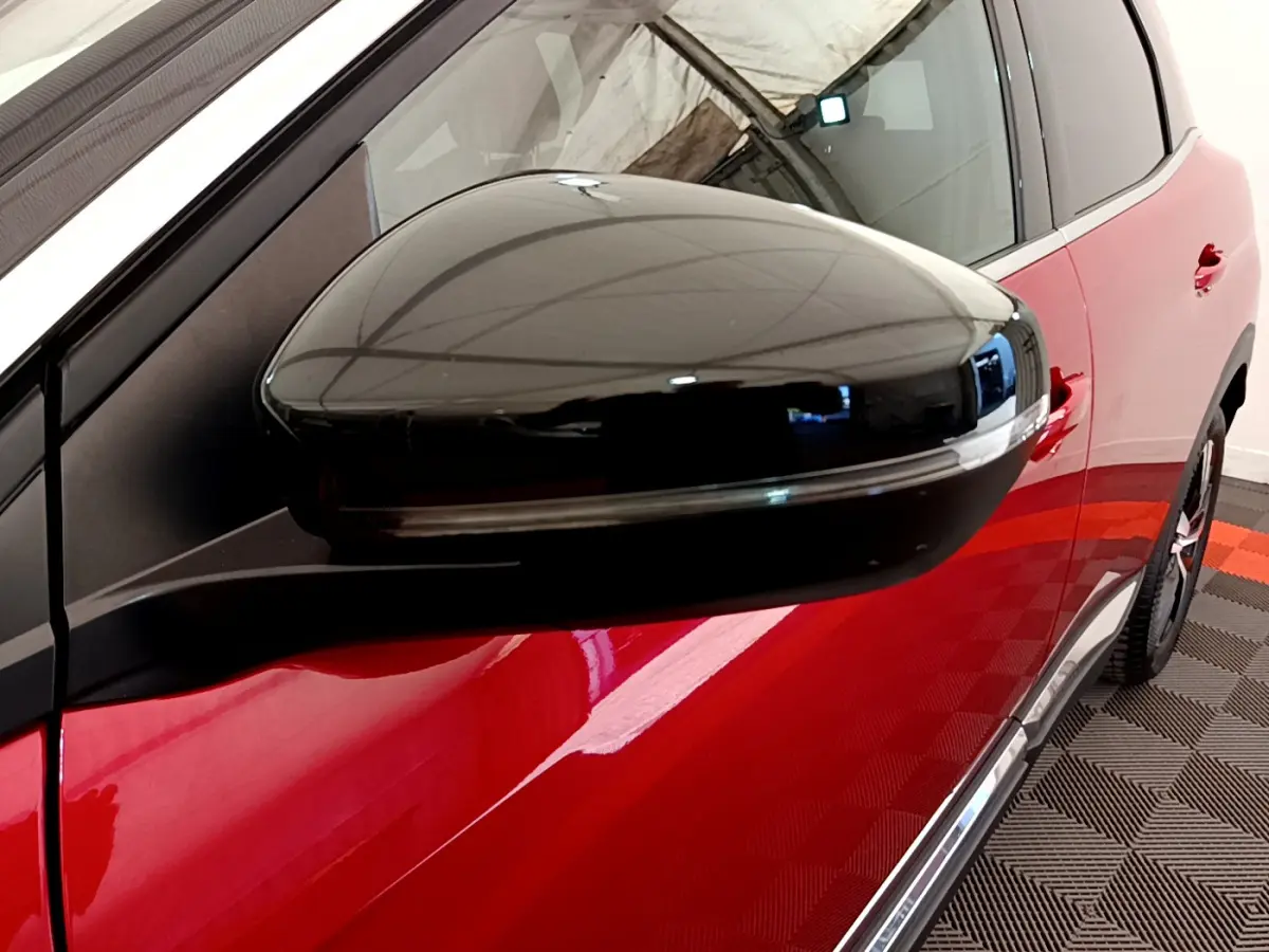 Gros plan sur le rétroviseur noir du côté gauche d'un Peugeot 3008 rouge brillant, vue latérale partielle.