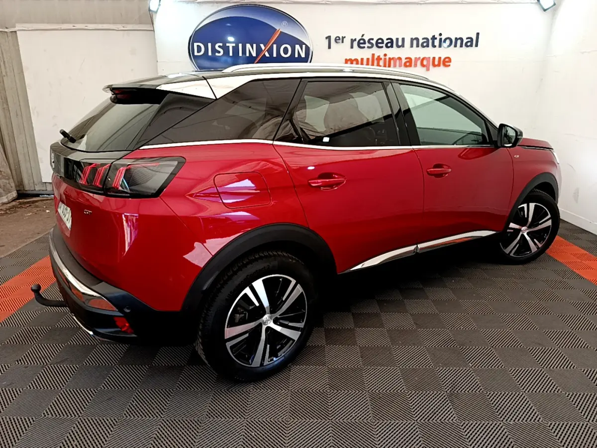 Vue 3/4 arrière droite d'un Peugeot 3008 GT rouge avec toit noir et jantes alliage bicolores dans un showroom.