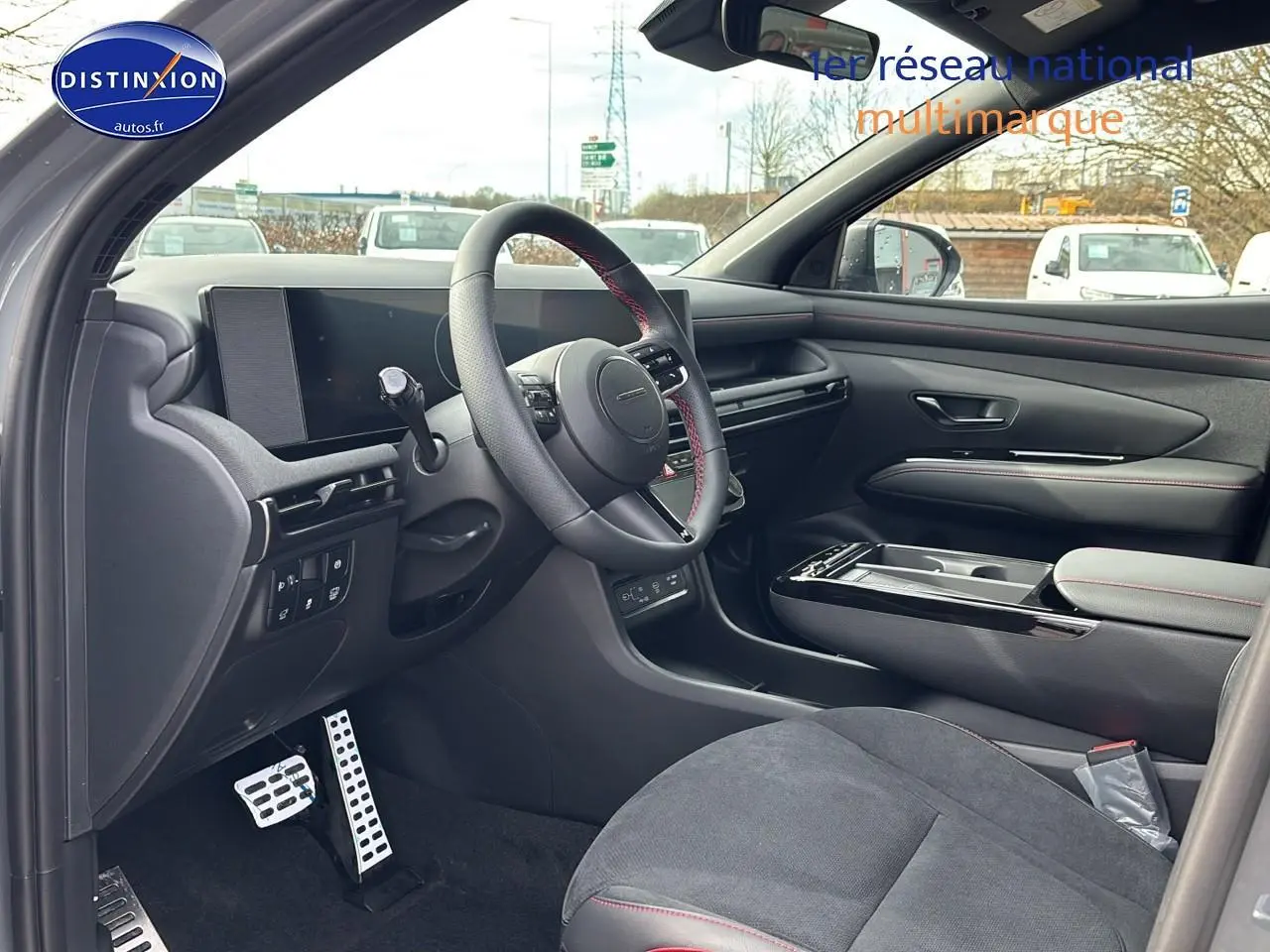Intérieur côté conducteur du Hyundai Tucson 2026 gris shadow, volant cuir avec surpiqûres rouges et tableau de bord numérique.