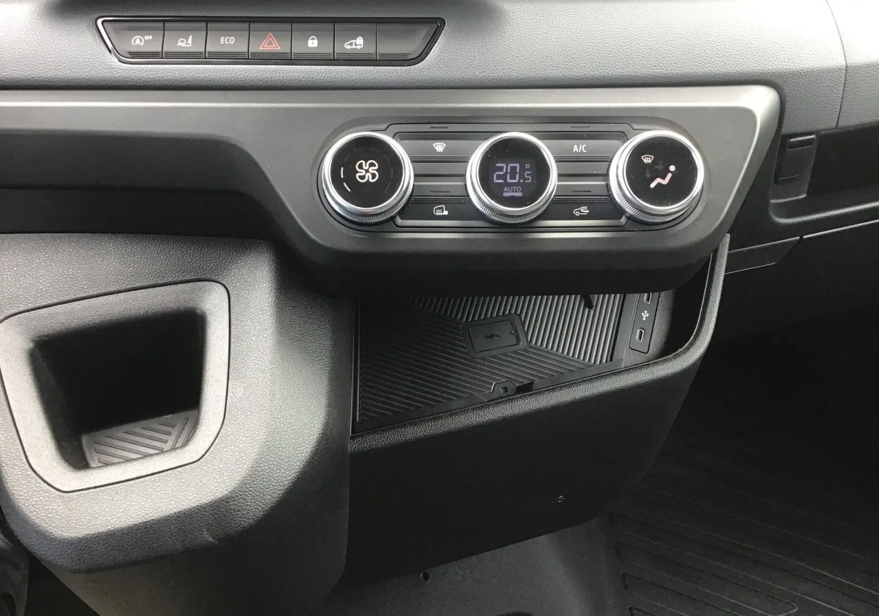 Détail de la console centrale du Renault Master blanc 2026 montrant les commandes de climatisation et un espace de rangement avec recharge smartphone par induction.