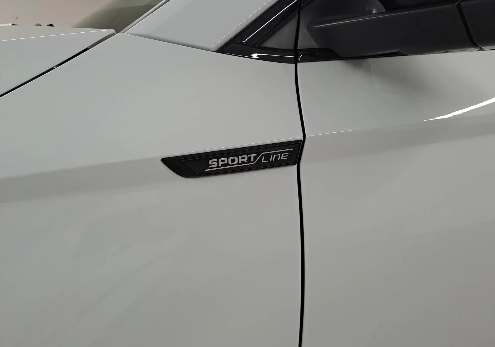 Gros plan sur l’aile avant gauche blanche lune du Skoda Karoq 2025 avec l’inscription Sportline noire.