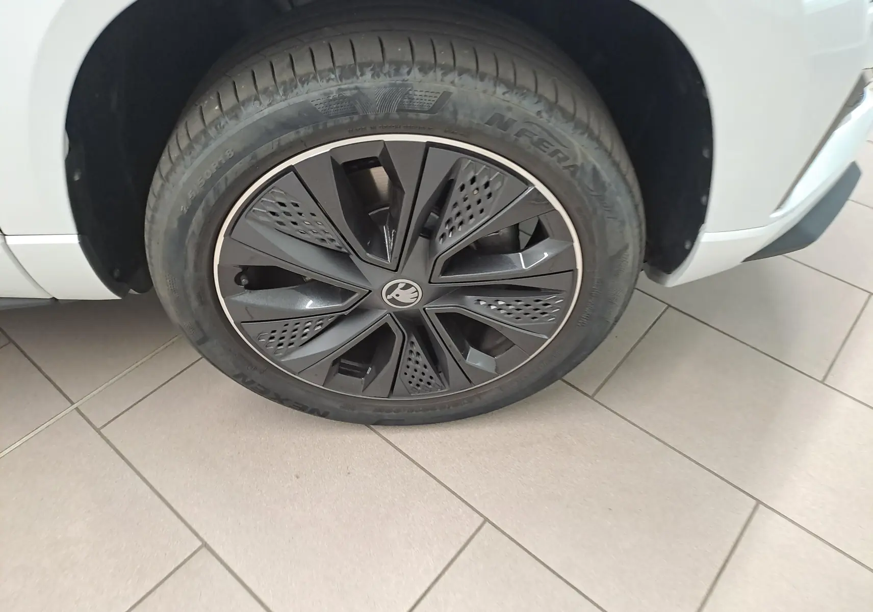 Gros plan sur la roue avant droite du Skoda Karoq 2025 blanc lune avec jante noire au design sportif.
