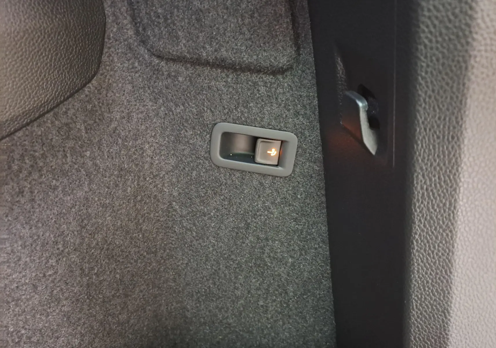 Bouton d'ouverture électrique du coffre sur moquette noire à l'intérieur d'un Skoda Karoq Blanc Lune 2025.