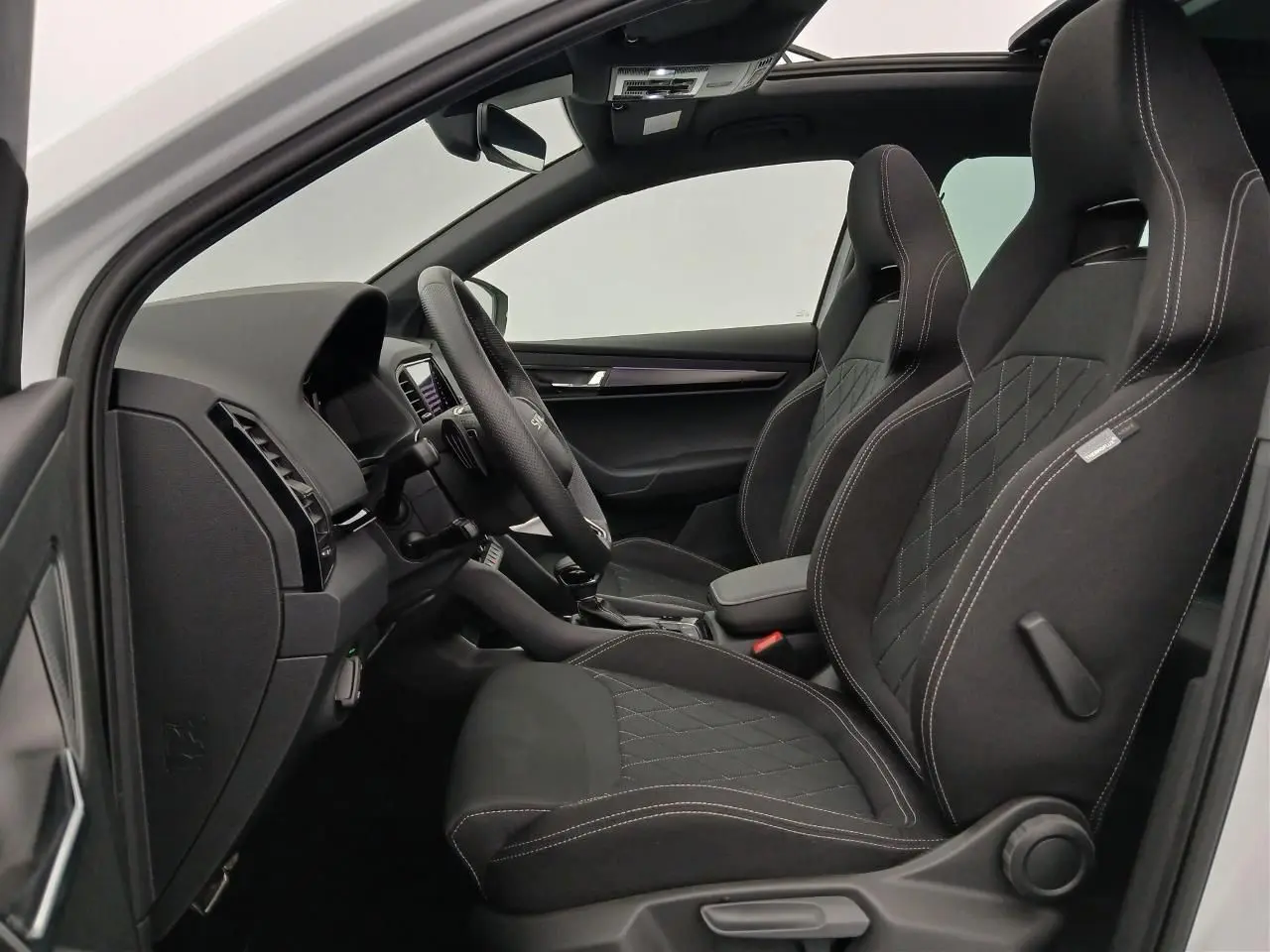 Vue intérieure côté gauche du Skoda Karoq 1.5 TSI 150 DSG7 Sportline 2025 en Blanc Lune, sièges sport noirs avec surpiqûres.