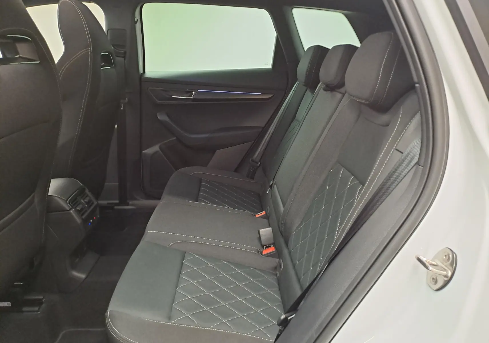 Vue intérieure côté gauche des sièges arrière noirs avec surpiqûres blanches du Skoda Karoq Blanc Lune 2025 version Sportline.