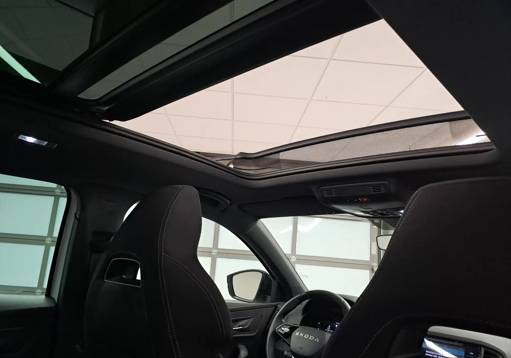 Intérieur du Skoda Karoq 2025 blanc lune, vue depuis l'arrière montrant les sièges sport noirs et le toit ouvrant panoramique.