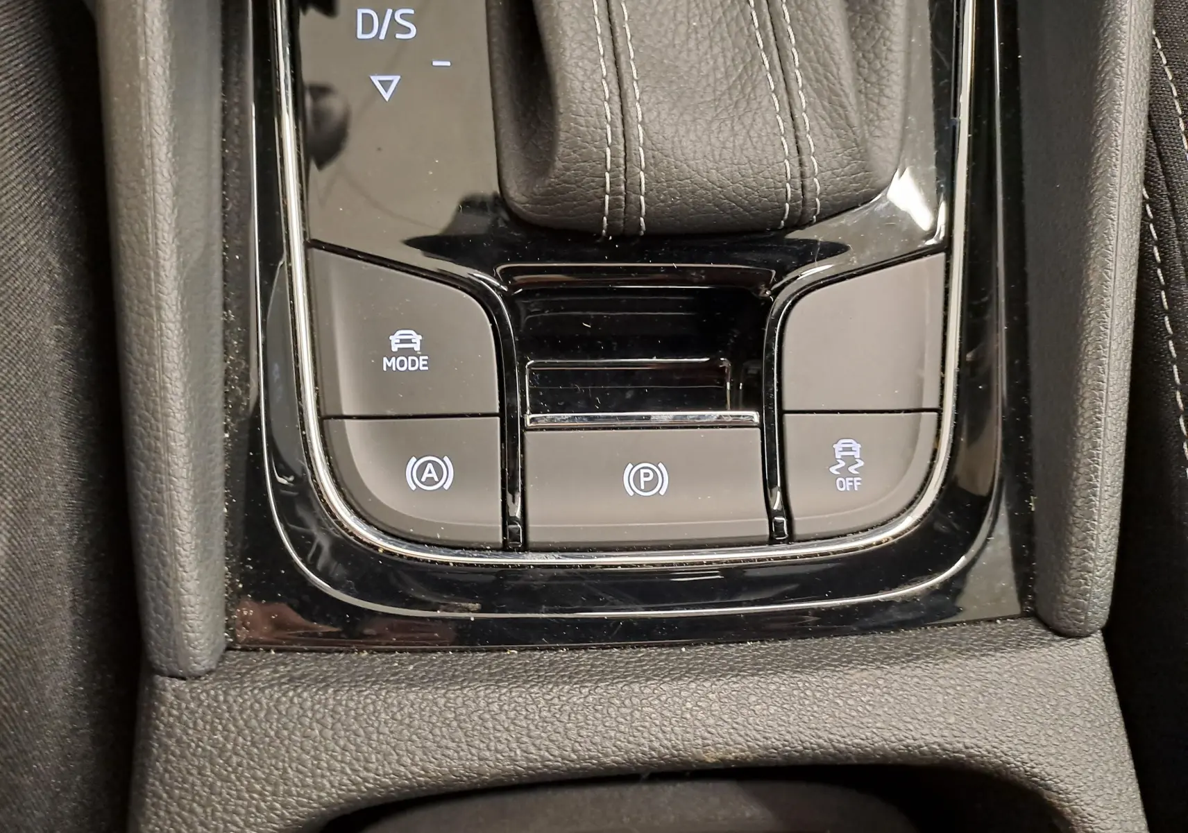 Gros plan sur la console centrale noire brillante du Skoda Karoq 1.5 TSI 150 DSG7 Sportline avec boutons de mode et frein à main électronique.