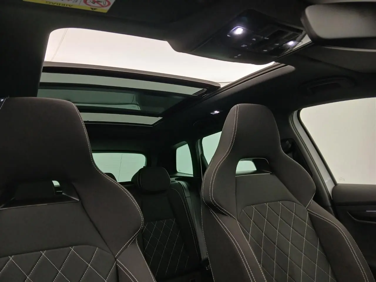 Intérieur du Skoda Karoq 2025 blanc lune, vue avant sur les sièges sport noirs avec surpiqûres blanches et toit panoramique ouvert.