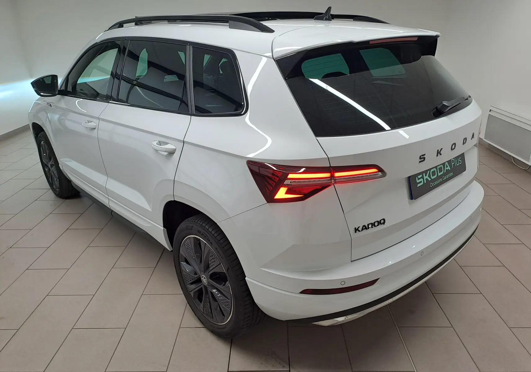 Vue 3/4 arrière droite du Skoda Karoq blanc lune 2025 avec feux LED allumés et jantes noires distinctives Sportline.