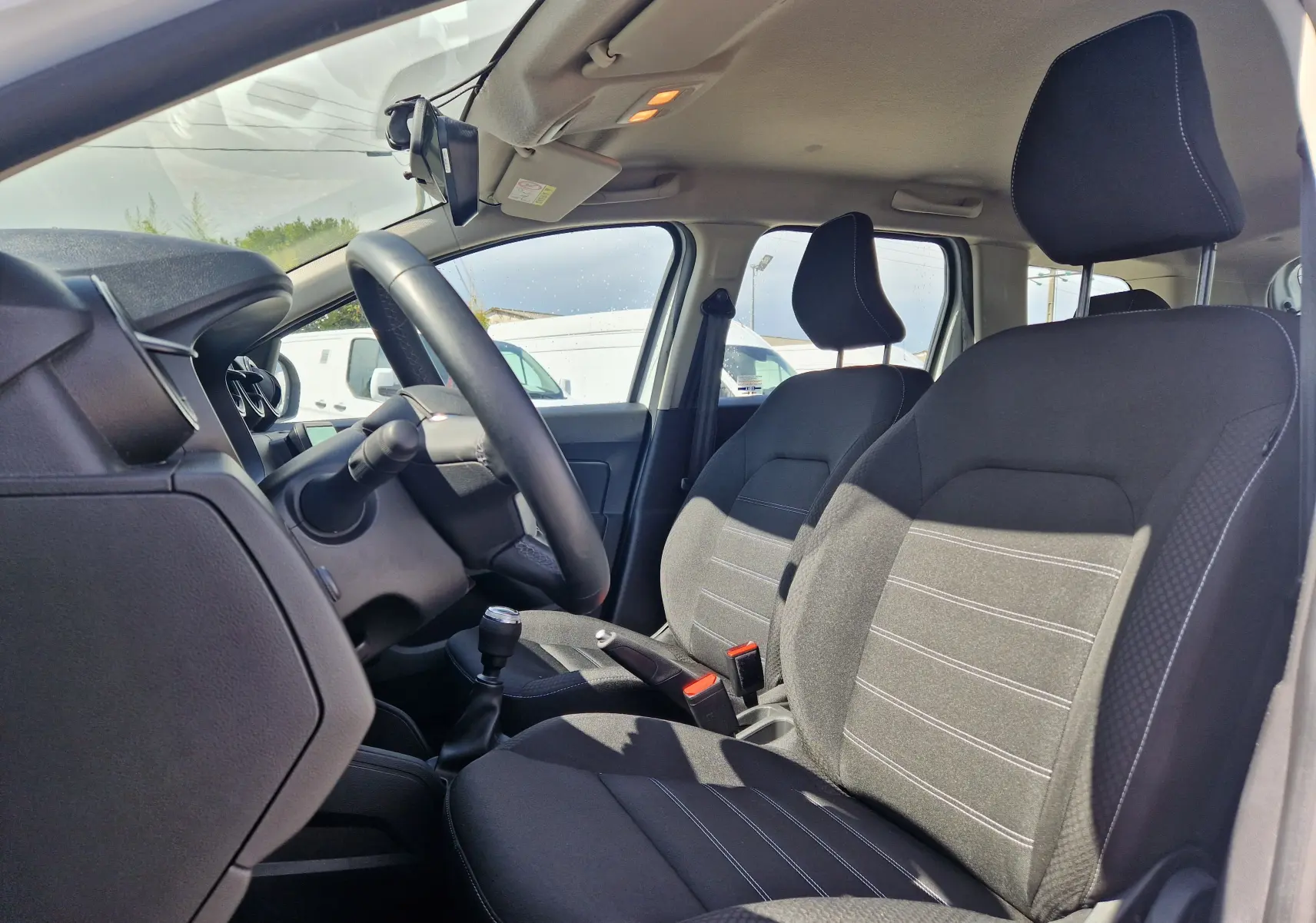 Intérieur du Dacia Duster 2023 vu côté conducteur, sièges noirs avec surpiqûres blanches et volant multifonction.