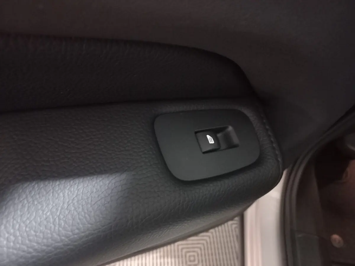 Gros plan sur le bouton de commande de lève-vitre arrière droit en plastique noir dans un Volvo XC60 gris clair 2022.