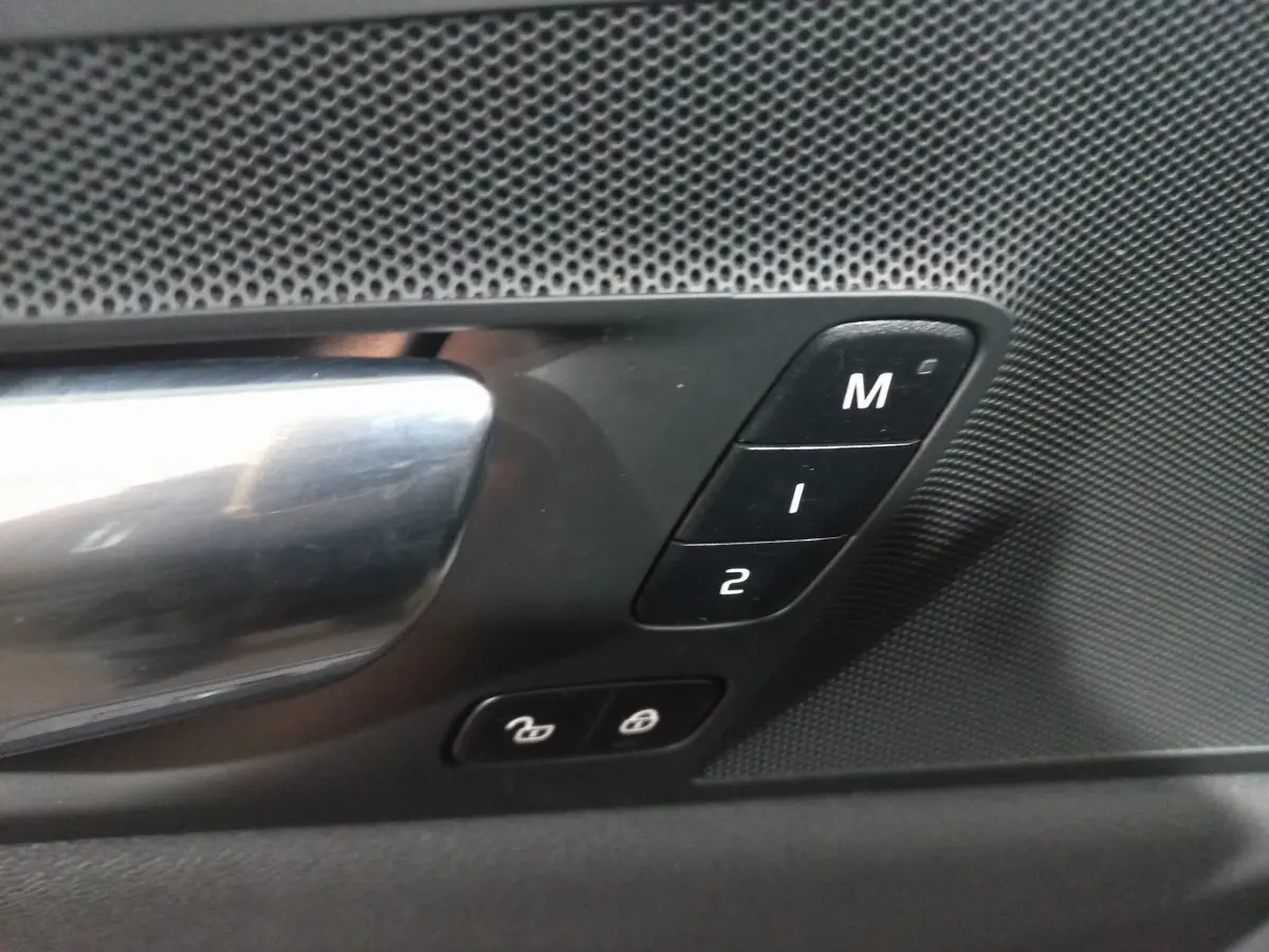 Gros plan sur la poignée de porte intérieure et les boutons de mémoire des sièges du Volvo XC60 gris clair 2022.