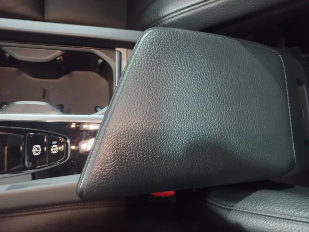 Gros plan sur l'accoudoir central en cuir noir et la console avec commandes électroniques du Volvo XC60 gris clair.