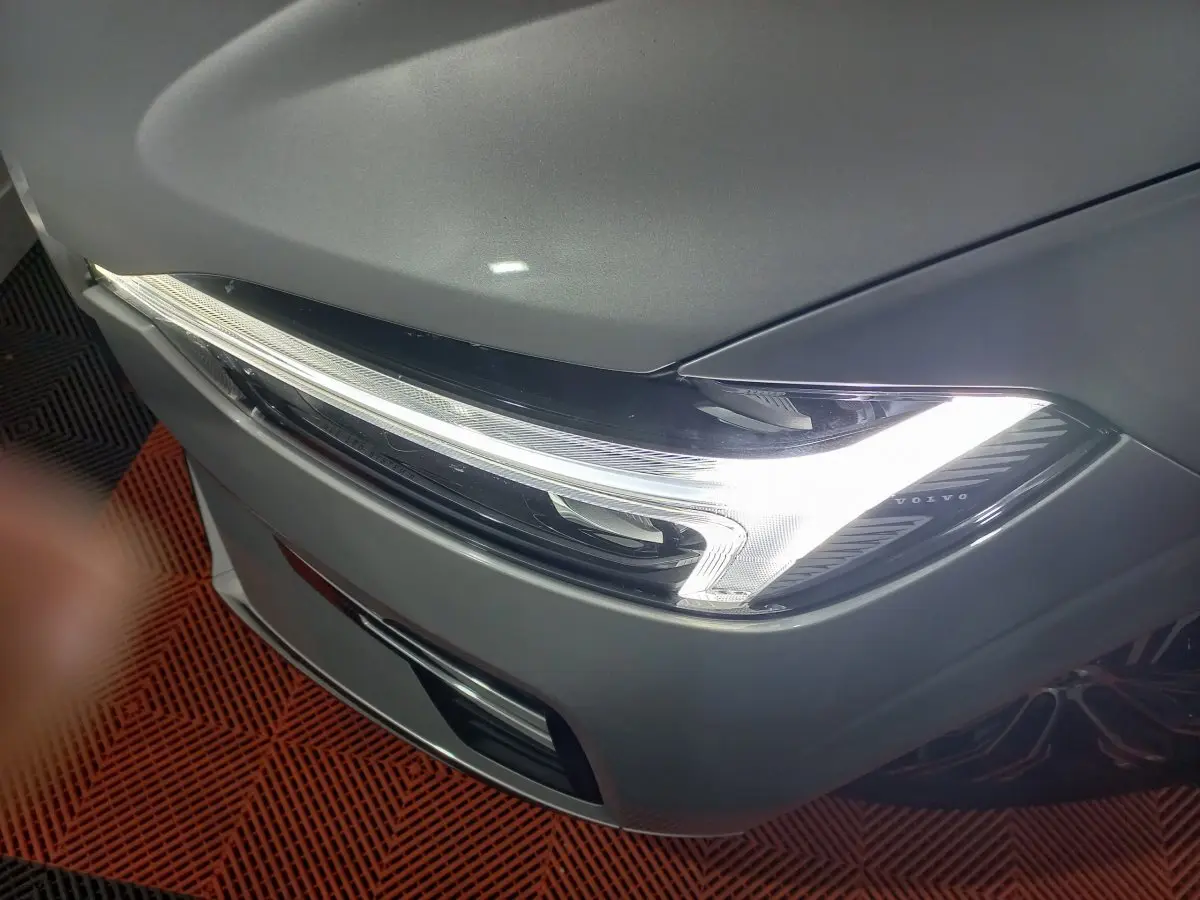 Gros plan sur le phare avant droit allumé d’un Volvo XC60 gris clair, soulignant son design LED distinctif.