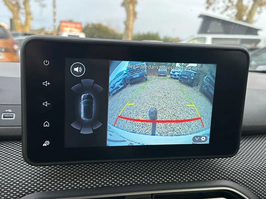 Écran intérieur montrant la caméra de recul avec guidage coloré sur un Dacia Sandero blanc, vue de face.