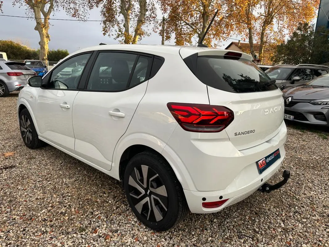 Vue 3/4 arrière droite d'une Dacia Sandero blanche 2024 avec feux arrière LED et attelage de remorque.
