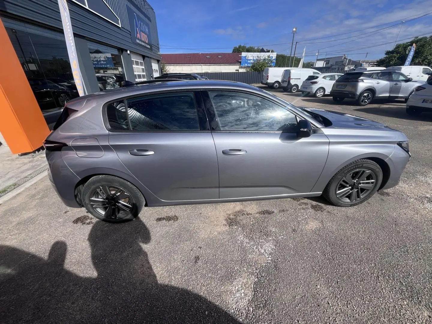 Profil droit d'une Peugeot 308 2024 gris Artense avec jantes alliage noires, garée en extérieur au soleil.
