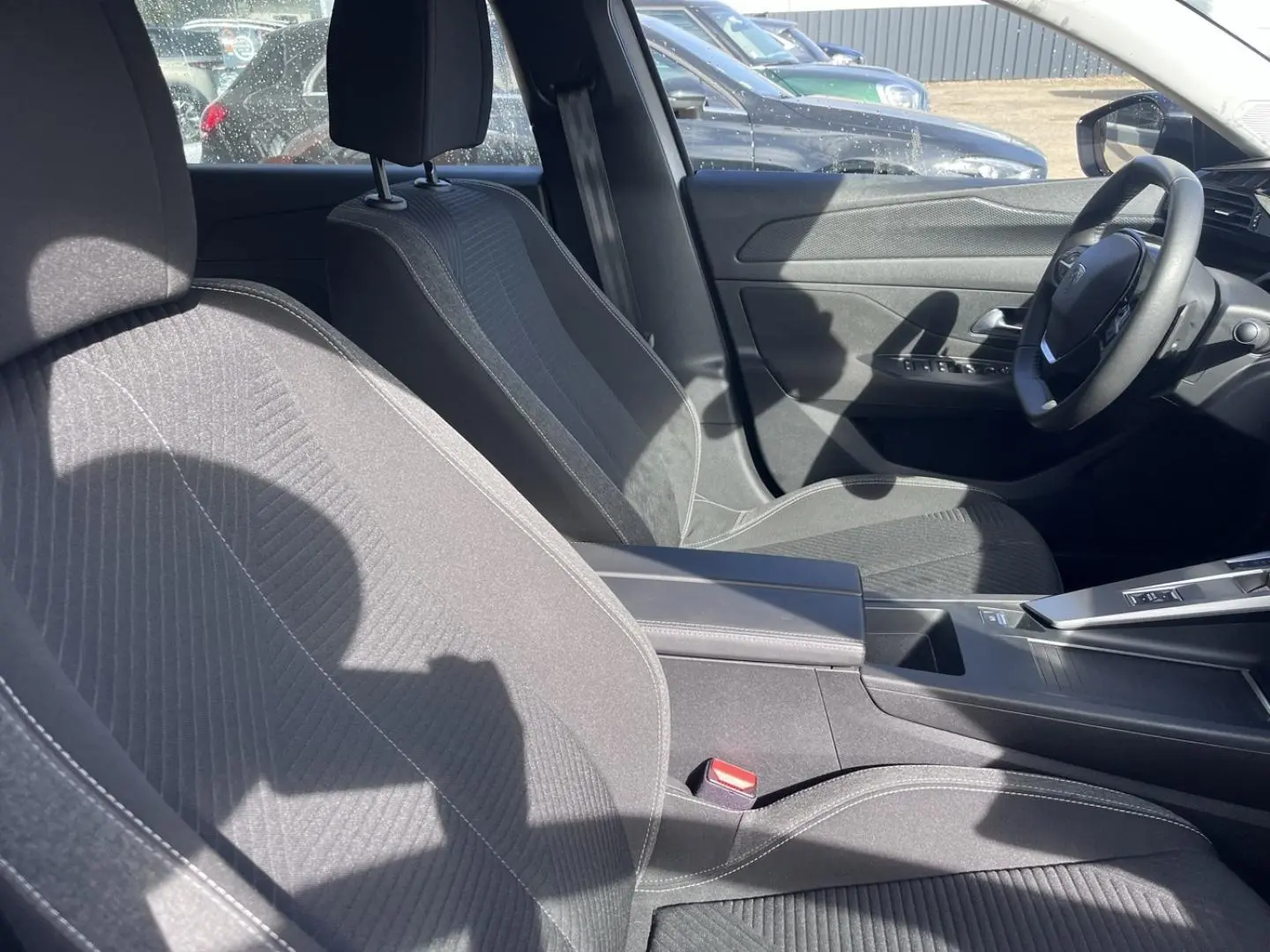 Intérieur avant de la Peugeot 308 2024, vue côté droit sur sièges tissu gris et console centrale avec accoudoir.