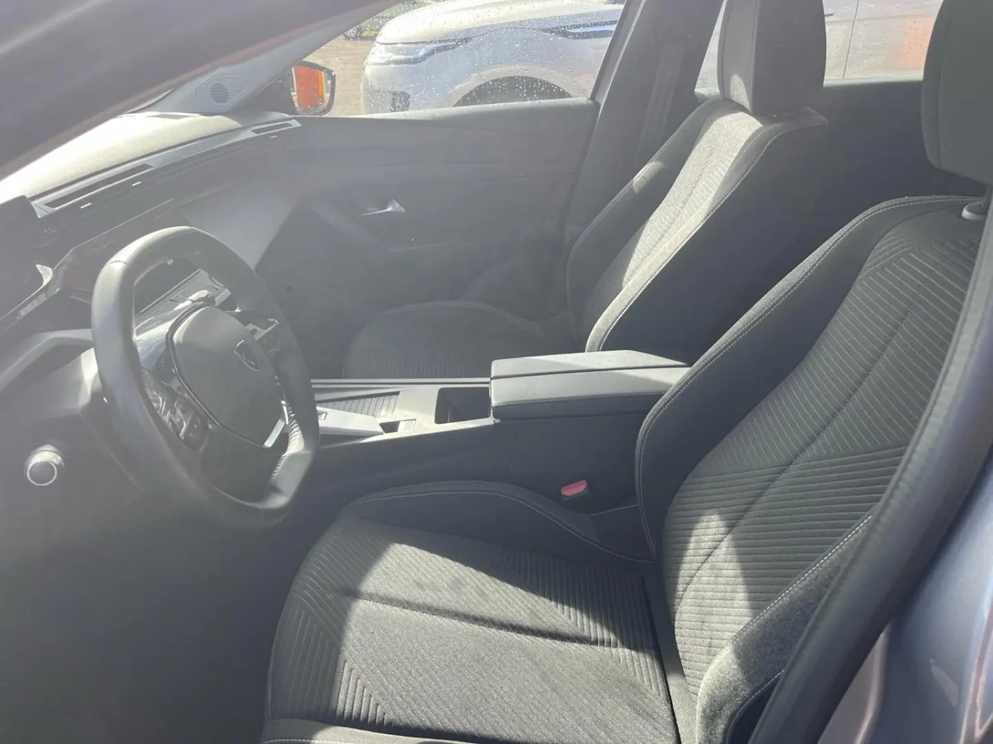 Vue intérieure côté conducteur de la Peugeot 308 2024, sièges tissu gris et volant multifonction noir.