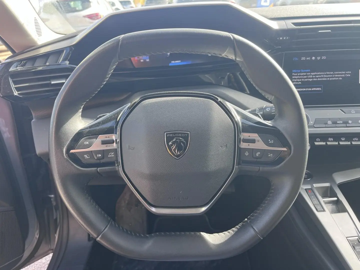 Vue rapprochée du volant multifonction noir avec logo Peugeot, tableau de bord et écran tactile en arrière-plan.