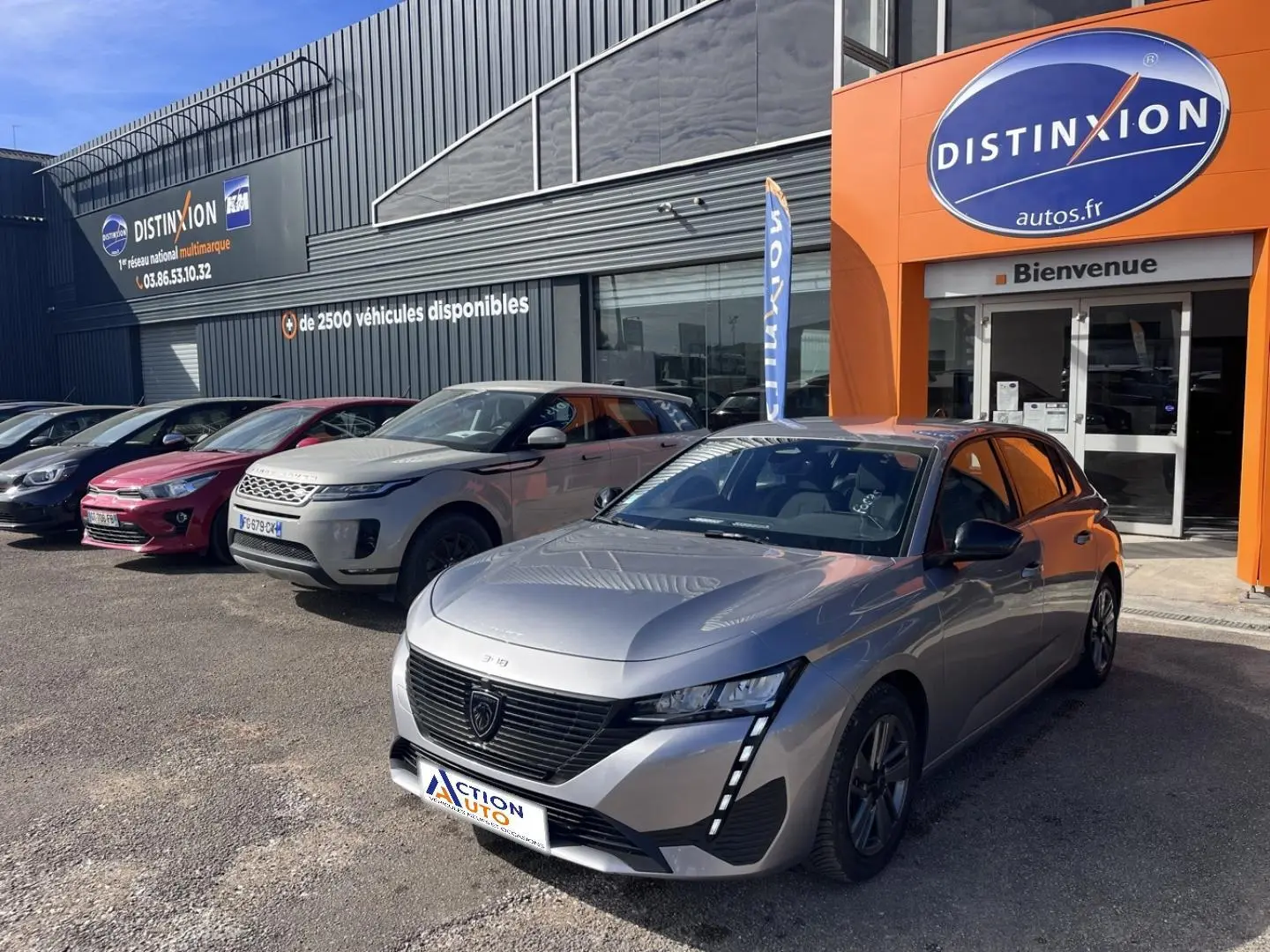 Peugeot 308 gris Artense vue 3/4 avant droit, avec calandre noire et feux LED verticaux, devant concession Distinxion.
