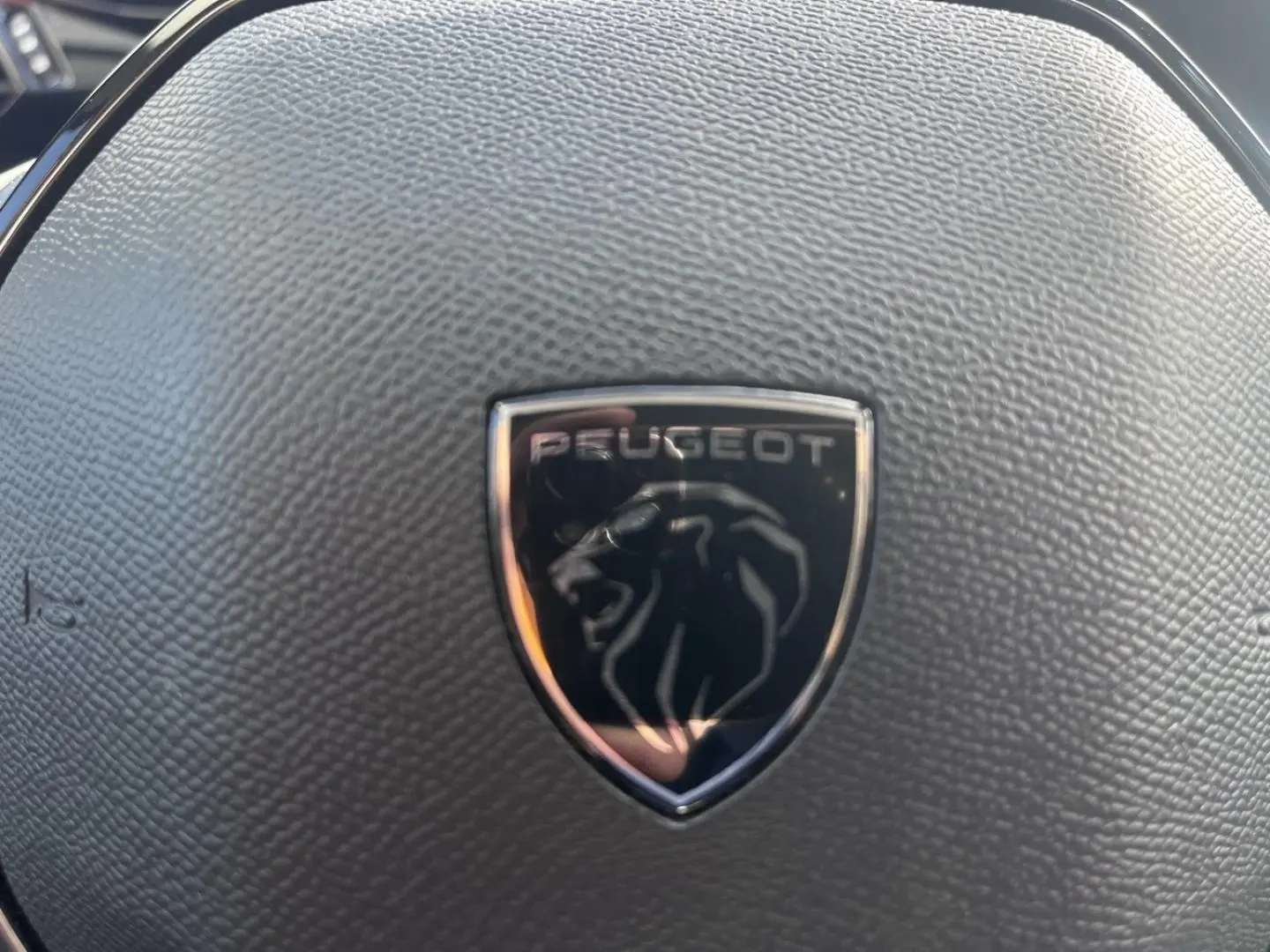 Gros plan sur le volant noir texturé avec logo Peugeot en relief au centre, intérieur de la Peugeot 308 2024.