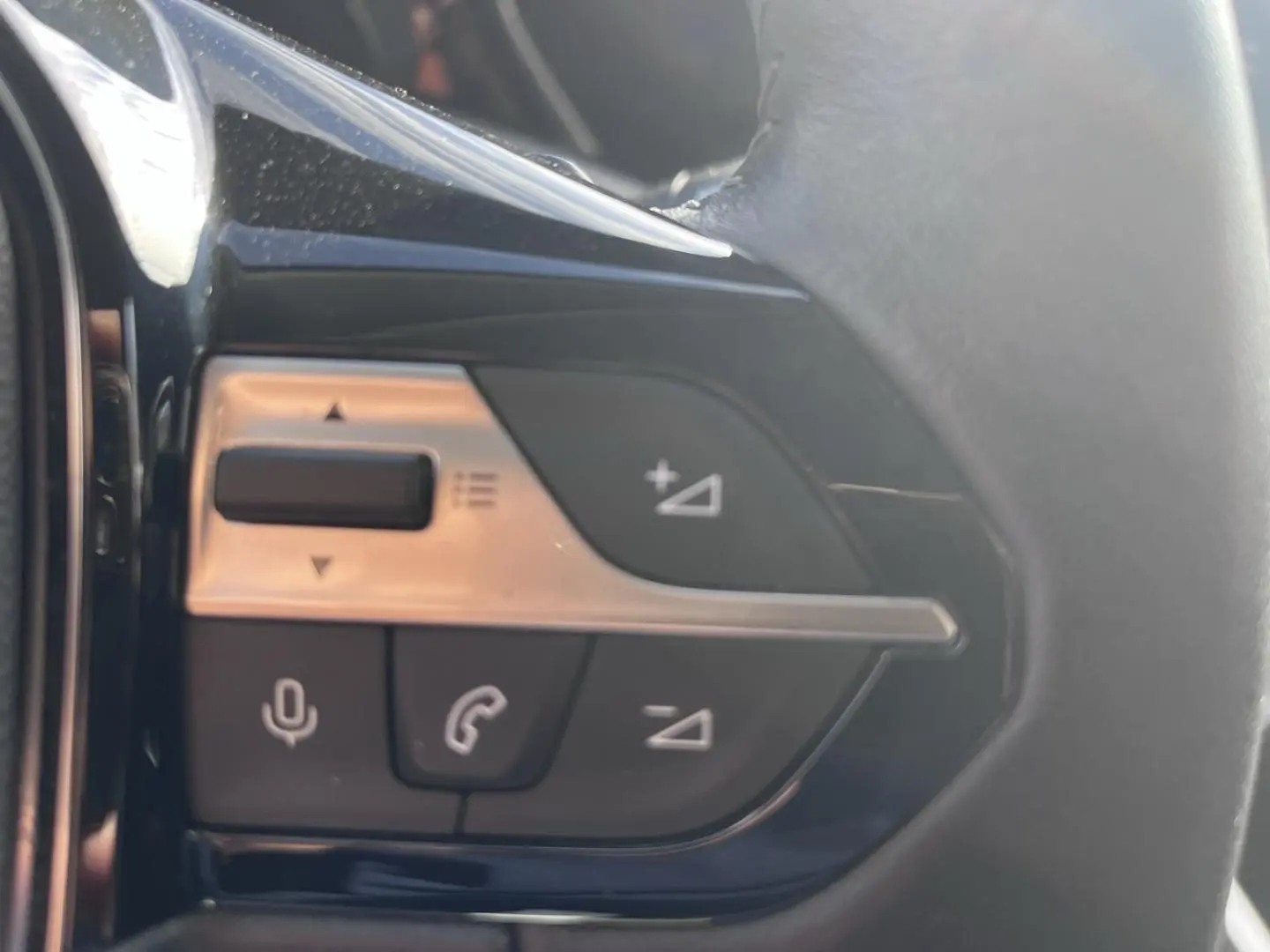 Gros plan sur les commandes multifonctions au volant noir de la Peugeot 308 2024, version essence gris Artense.