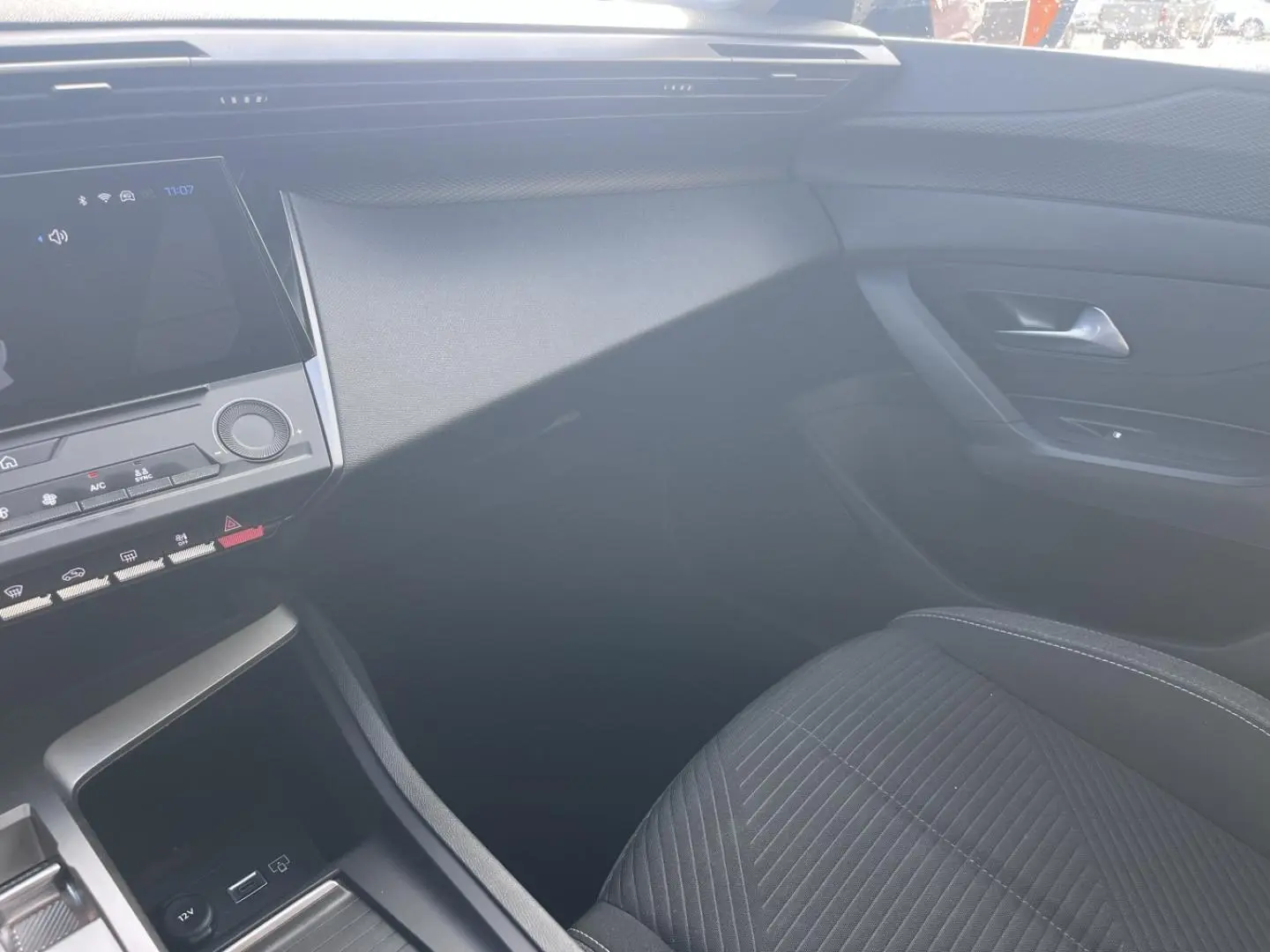 Vue intérieure côté passager de la Peugeot 308 2024 avec siège tissu noir et tableau de bord moderne.