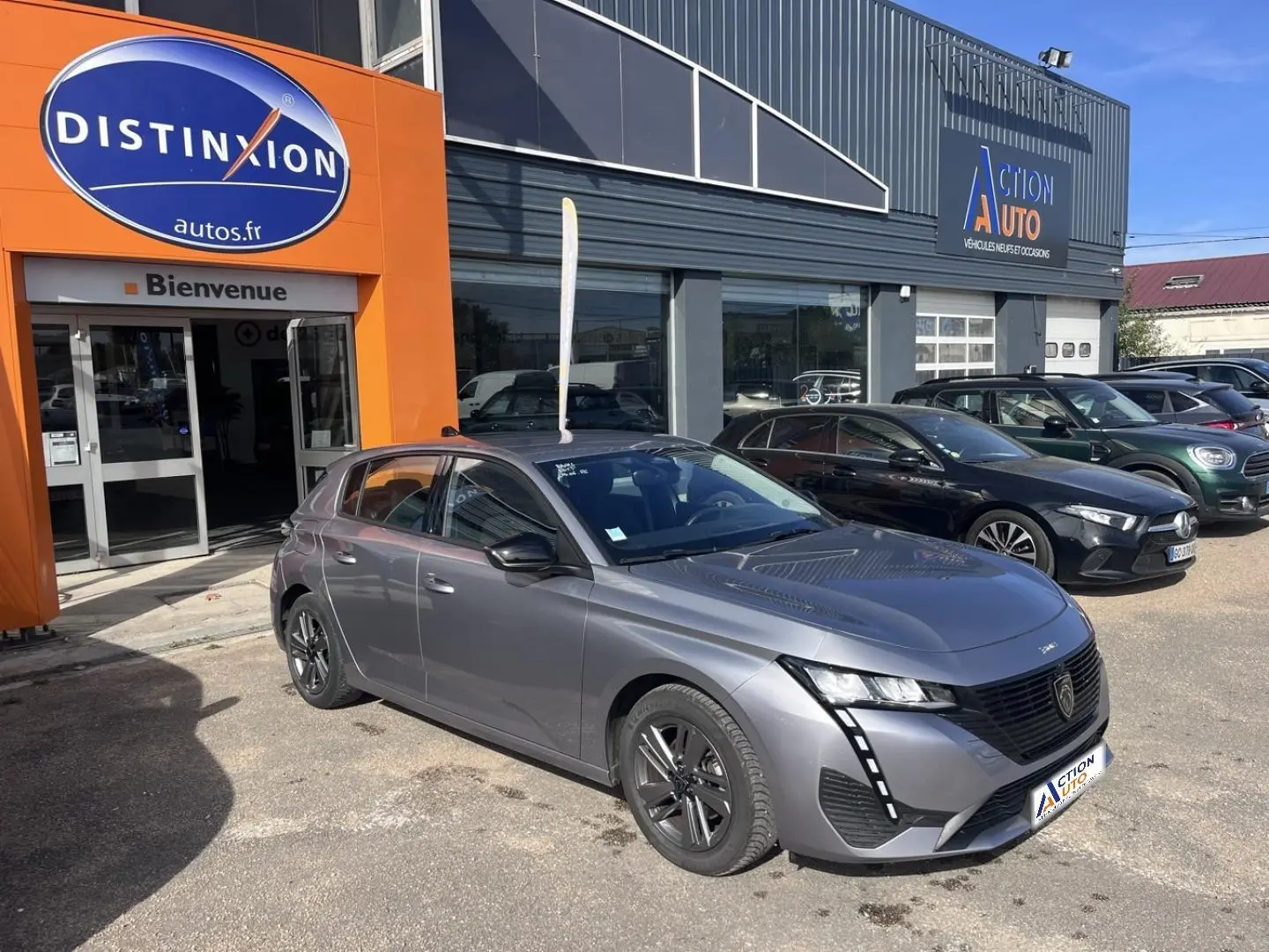 Peugeot 308 gris Artense vue 3/4 avant droit, avec jantes noires et feux LED distinctifs, devant un garage.