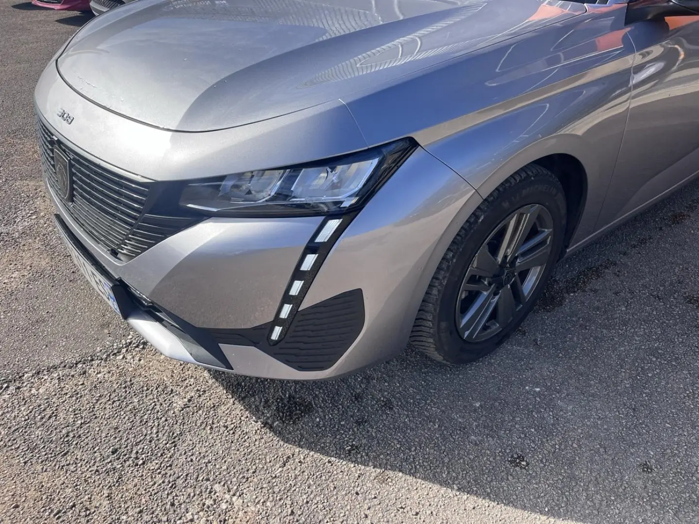 Vue 3/4 avant droit d'une Peugeot 308 gris Artense avec phares LED et calandre noire distinctive.