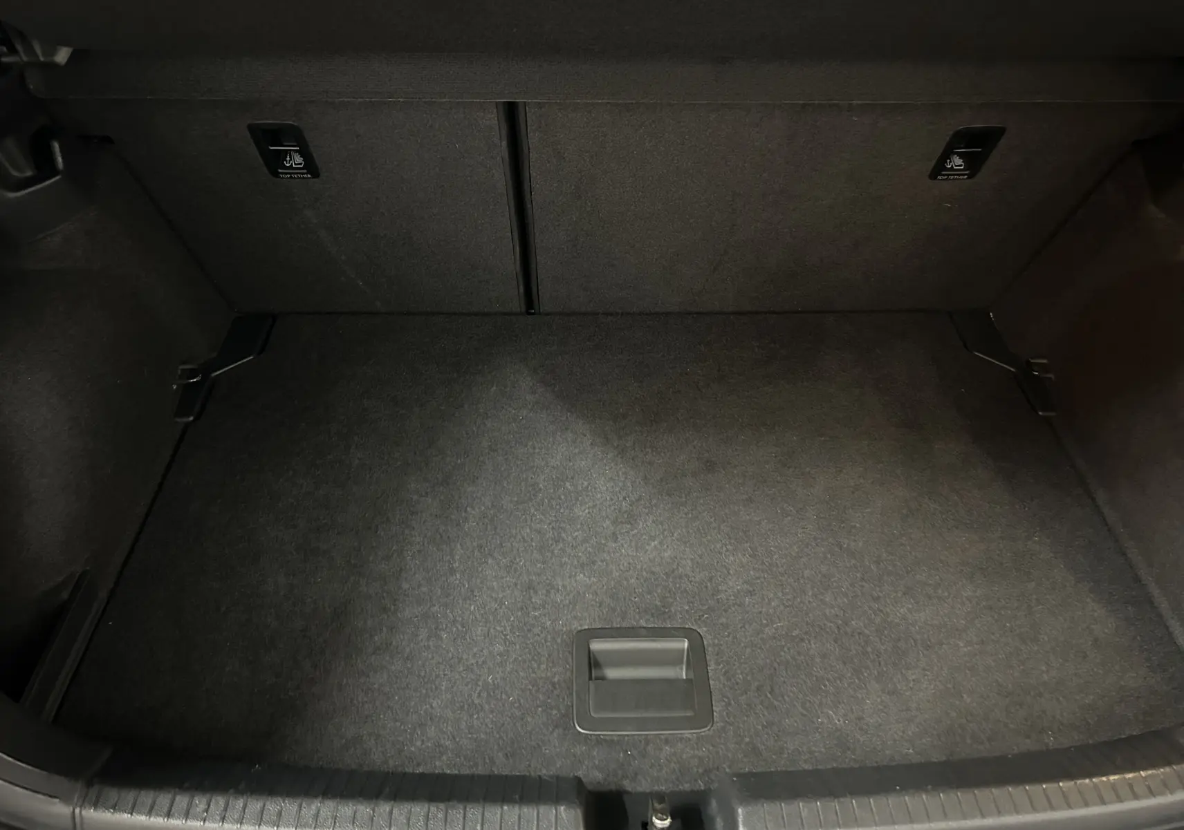 Vue plongeante sur le coffre noir vide de la Volkswagen Polo 2022, montrant la moquette et les ancrages Isofix.