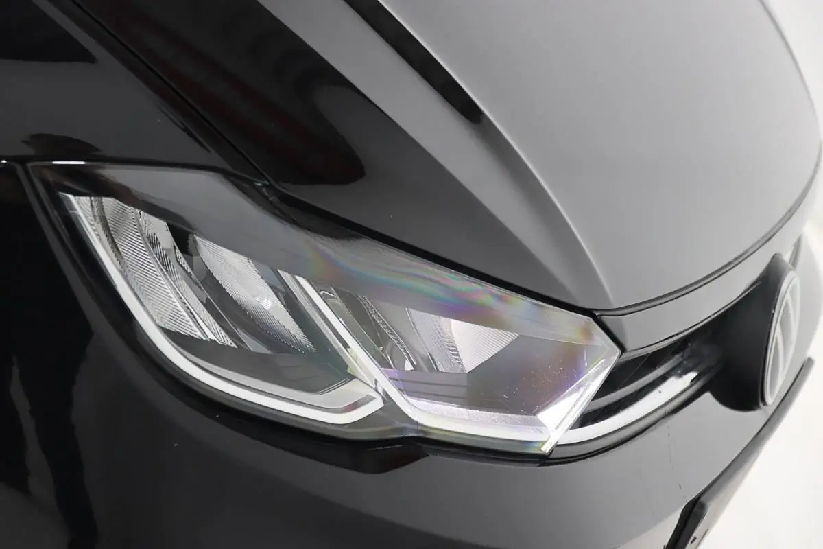 Gros plan sur le phare avant gauche noir brillant d'une Volkswagen Polo 2022 avec logo VW visible.