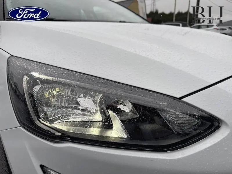 Gros plan sur le phare avant gauche d'une Ford Focus SW 1.5 EcoBlue blanc glacier sous la pluie.
