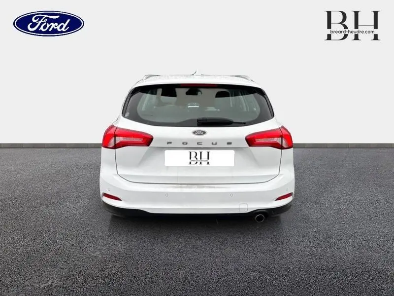 Vue arrière d'une Ford Focus SW blanche Glacier de 2020 avec feux arrière rouges et sortie d'échappement chromée visible.