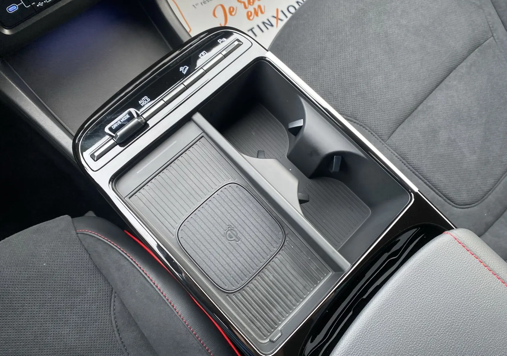 Vue plongeante sur la console centrale noire du Hyundai Tucson gris, avec porte-gobelets et accoudoir en cuir noir à surpiqûres rouges.