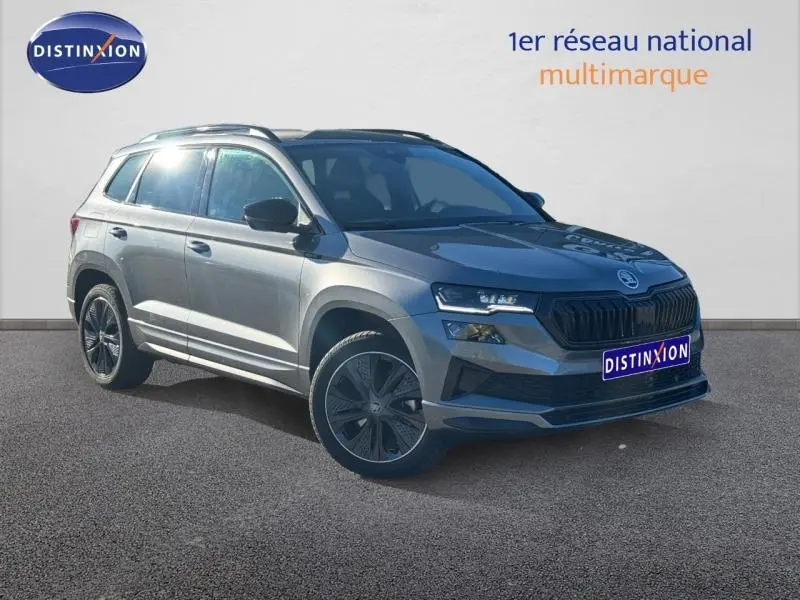 Vue 3/4 avant droit d’un SKODA KAROQ gris perle avec jantes alliage noires et toit équipé de barres de toit.
