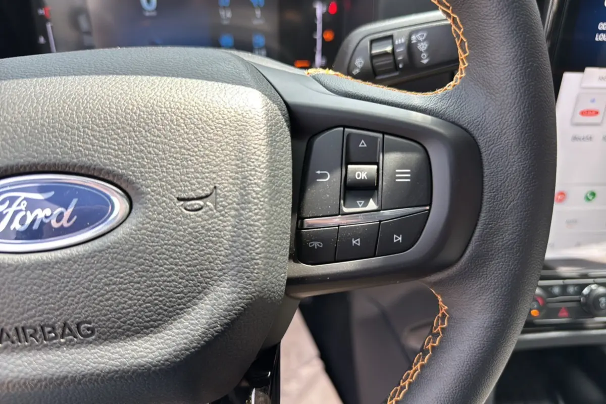 Gros plan sur le volant cuir noir avec surpiqûres orange du Ford Ranger Wildtrak 2026, boutons multifonctions visibles.
