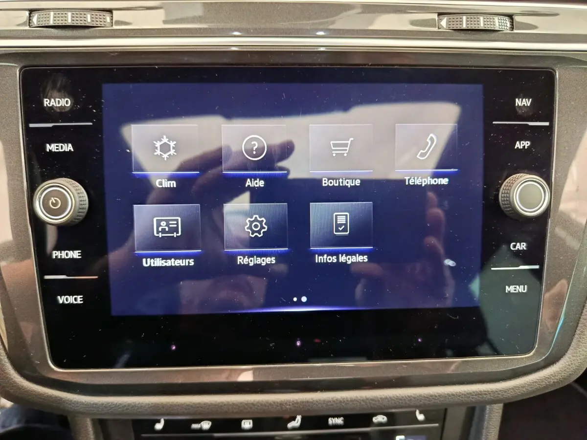 Écran tactile central du Volkswagen Tiguan 1.4 eHybrid 2023 affichant le menu principal avec options clim, aide, boutique et téléphone.