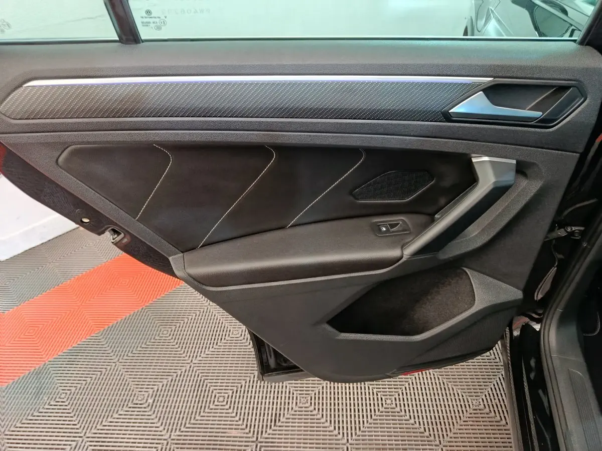 Vue intérieure de la porte arrière droite noire du Volkswagen Tiguan 1.4 eHybrid 2023 avec surpiqûres blanches et insert carbone.