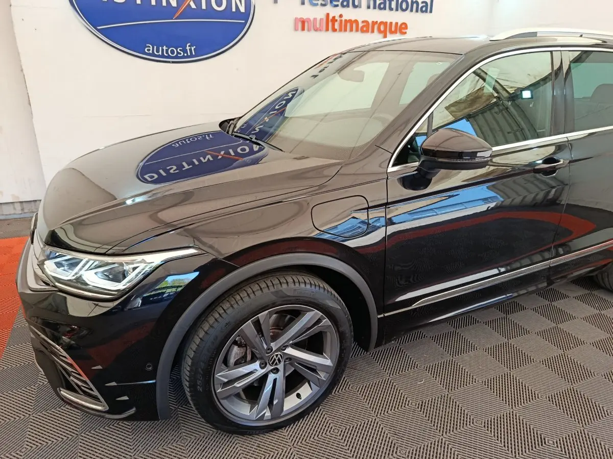 Vue de trois quarts avant droit du Volkswagen Tiguan noir 1.4 eHybrid avec jantes alliage et prise de recharge latérale.